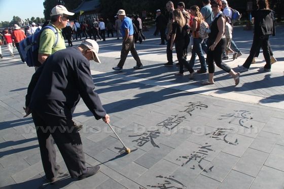 An old man writing chinese calligraphy with a big brush dipped in water 