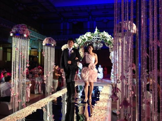 Here come the three pairs of bridemaids and best men arm in arm walking to the planform through the love corridor.
