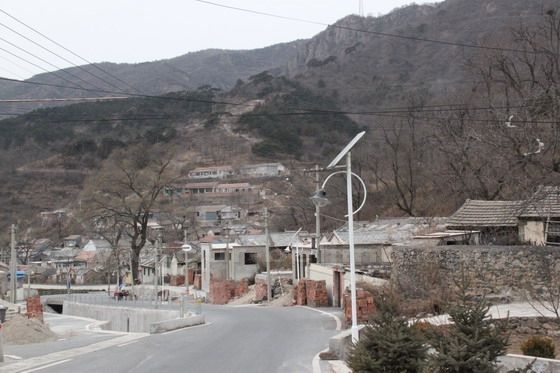 Parallelled by a gully, a wide main road passes through the village with solar-powered street lights. Farmhouses perched on the hillsides orderly