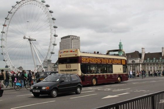 The Big Bus is passing a bridge over the Thames River with the background of the Eye of London