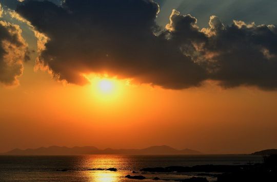 The rising Sun is up under clouds.