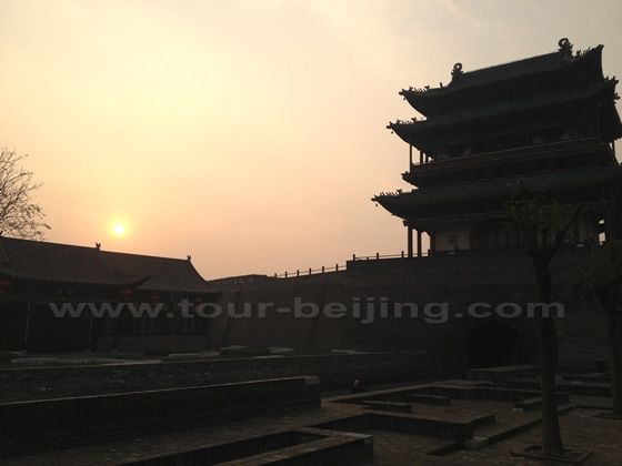 The rusing sun is appearing over the left shoulder of the multi-floor tower atop the South Gate.