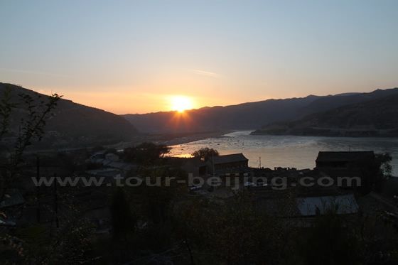 The sun is setting over the undulating mountain  and  the narrow riverbed of the Yellow River 