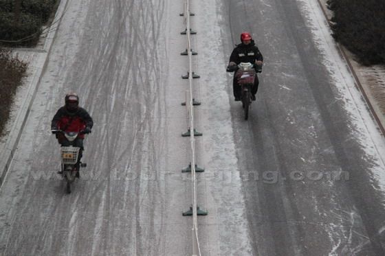 Two electric bike riders are braved the cold wind on the snow sidewalk