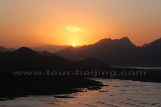 the rising sun half over the mountain line in the distance